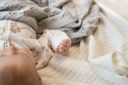 Baby with its hand up. Covered in grey blanket.