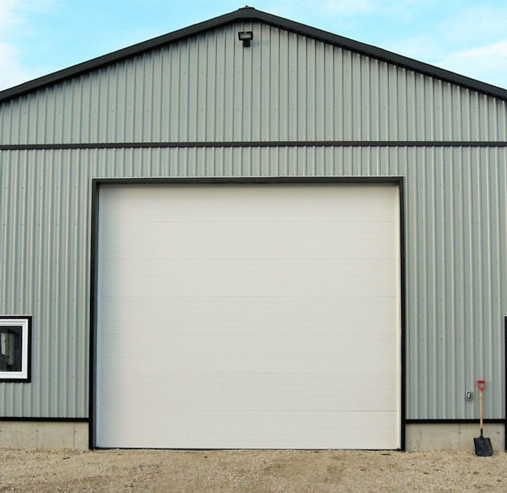 Light gray steel building with white overhead door and metal siding.