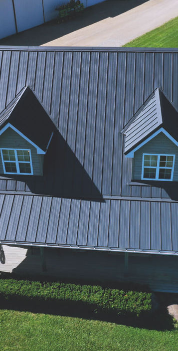 Aerial view of home with dark gray metal roof and twin dormer windows.