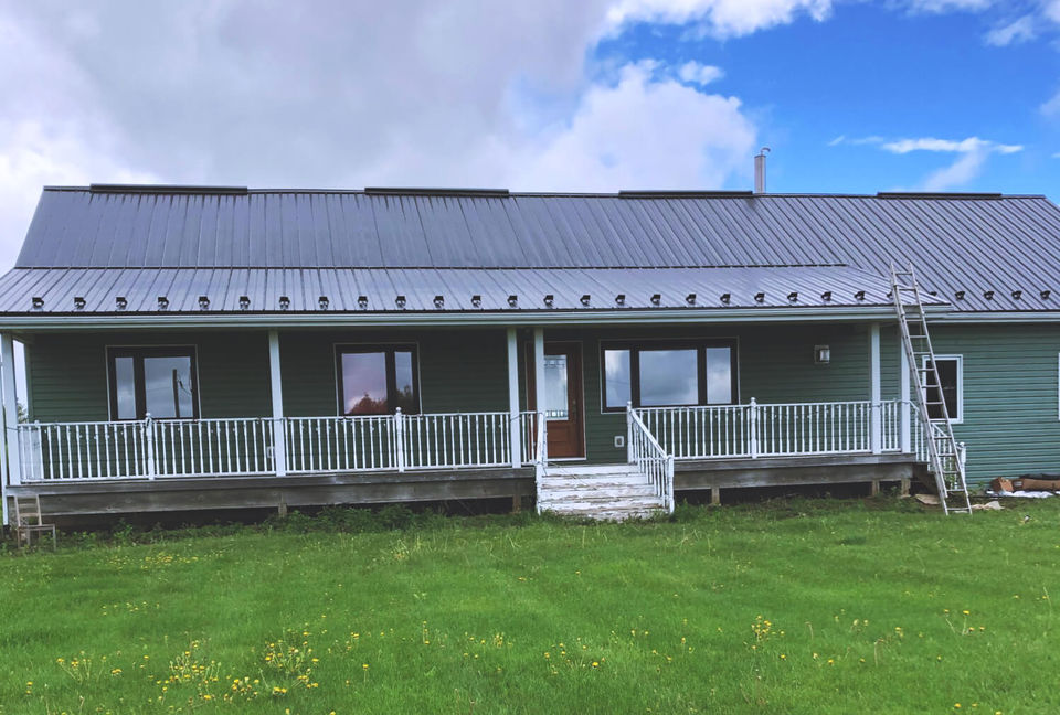 Country-style home with gray metal roof, covered front porch, and white railing on green lawn.
