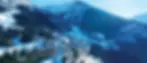 Snowy mountain village resort of Oz 3300 with wooden cabins, surrounded by pine trees. Ski slopes visible. Bright, clear sky above. Quiet, serene atmosphere.