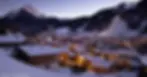 Snow-covered village of Morzine at dusk with illuminated houses nestled in a valley. Majestic mountains, ski slopes, and a serene winter vibe.