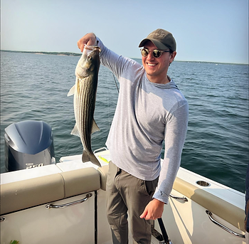 A man on a boat holding a large striped bass he just caught while fishing.