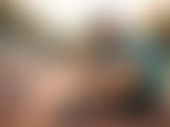 Man in blue shirt sits on track, looking tired. Shoes and water bottle beside him. Background shows trees and a jogging person at sunset.