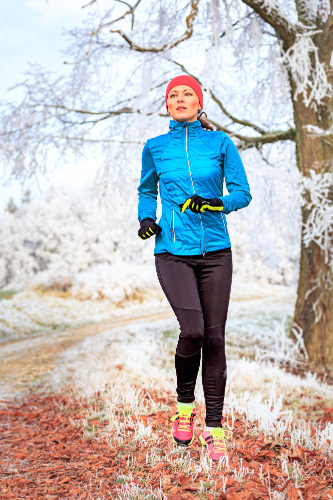 runner corre nel bosco con ghiaccio e neve e giacca blu