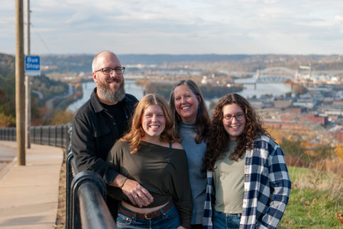 Family smiling while sitting in grass with fall leaves.