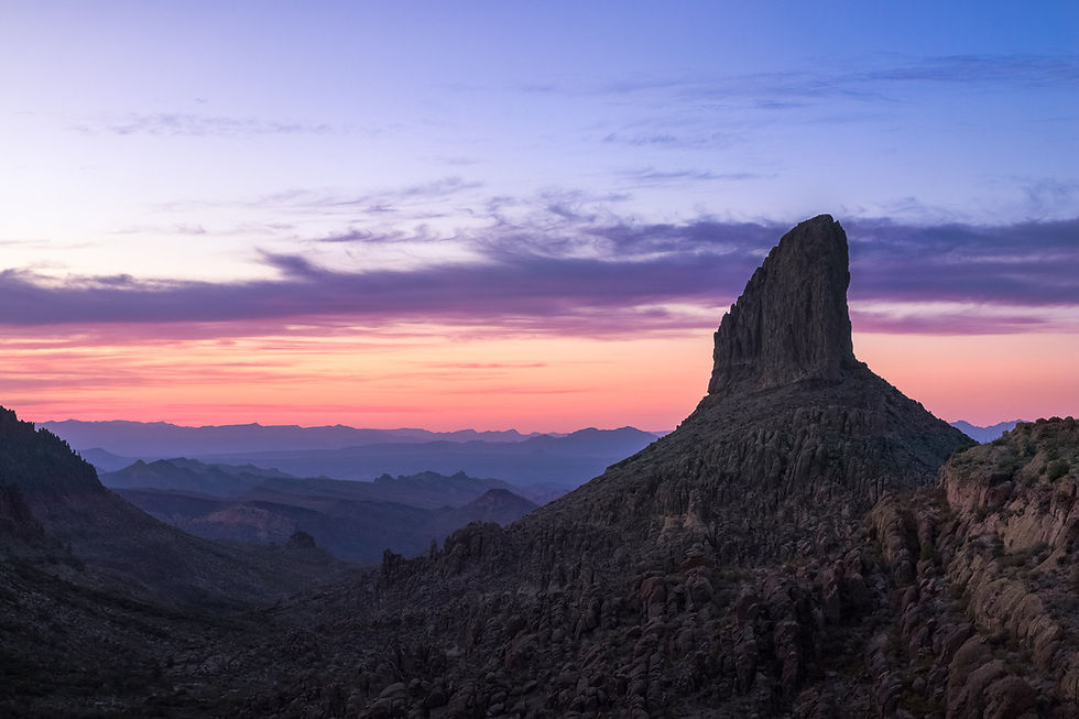 Silhouette of Weavers Needle at sunset with pastel hues fading into the distant mountains. By Michael Rung Photography