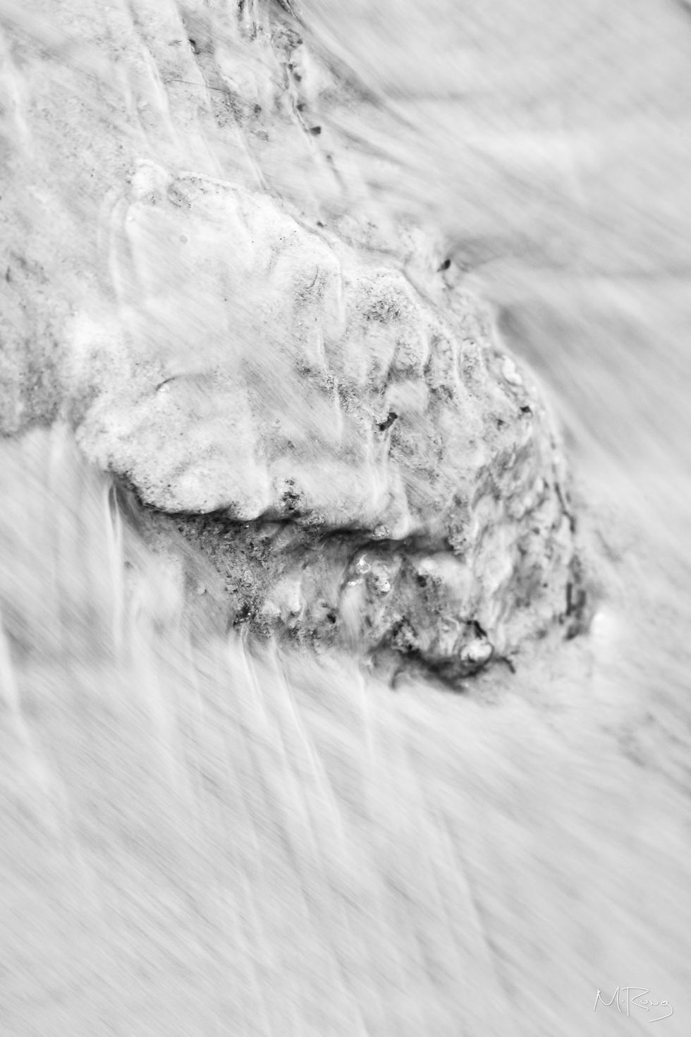 A long exposure black and white photo of water rushing over and around a rocky feature along the shore of Eagle Mountain Lake