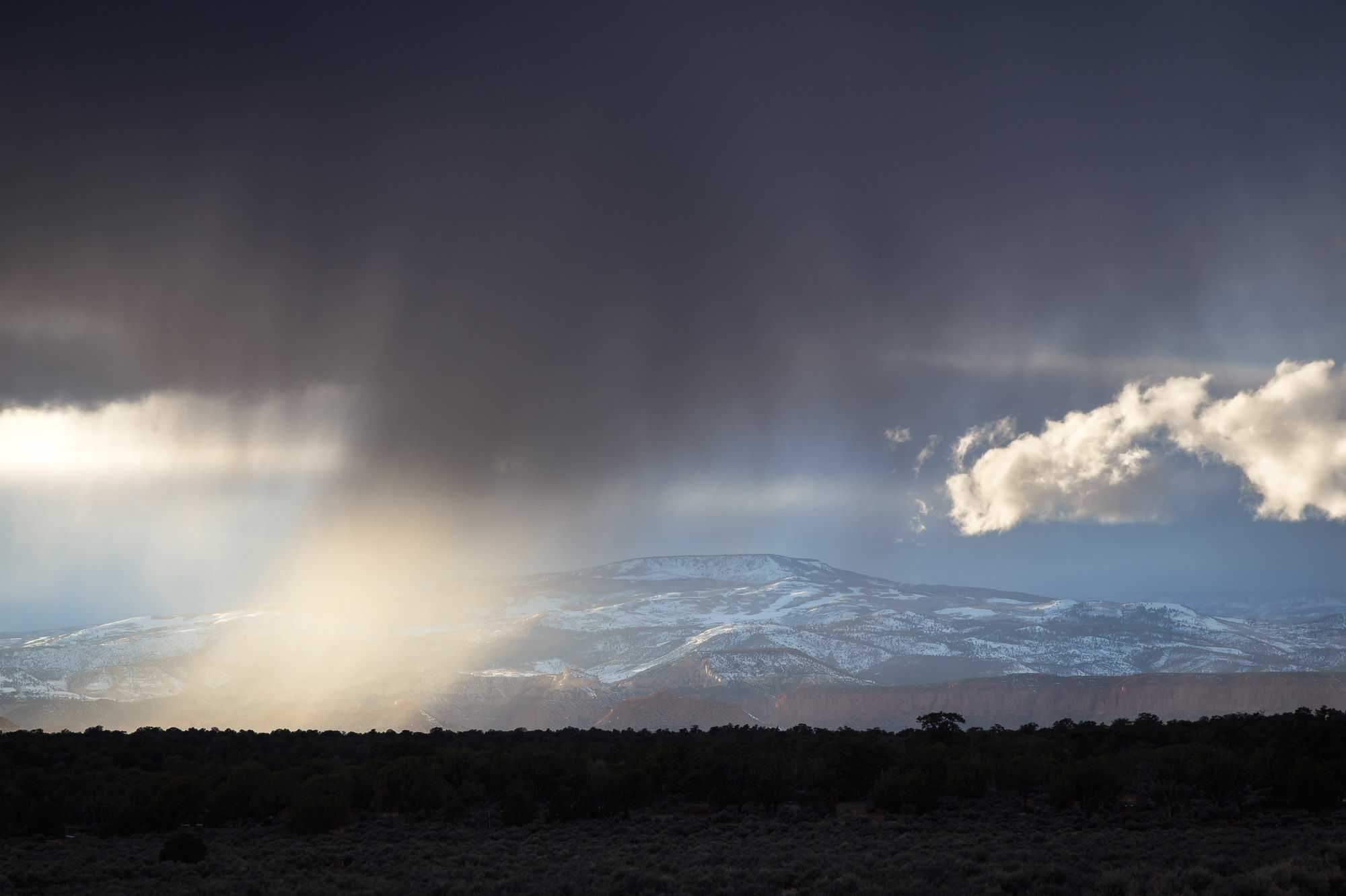 An afternoon snow shower, backlit by sunlit, falling over the Utah badlands outside Capitol Reef National Park