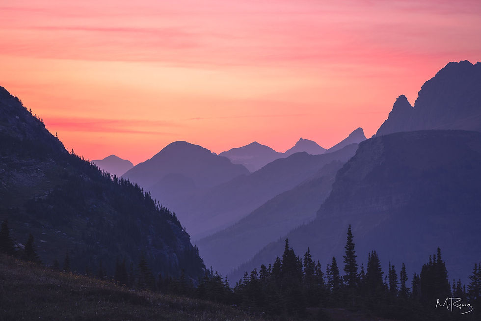Layers of silhouetted mountain peaks under a vibrant pink and orange sunset sky at Glacier National Park. By Michael Rung