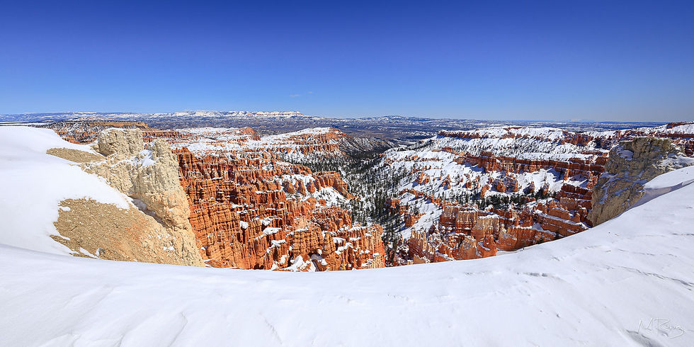 A panoramic view of Bryce Canyon in winter, framed by a curved snowdrift along the bottom of the photo