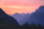 Layers of silhouetted mountain peaks under a vibrant pink and orange sunset sky at Glacier National Park. By Michael Rung