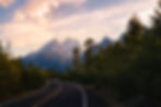 Sunset light hits the jagged Grand Teton mountain peaks as the road winds into the distance. By Michael Rung Photography