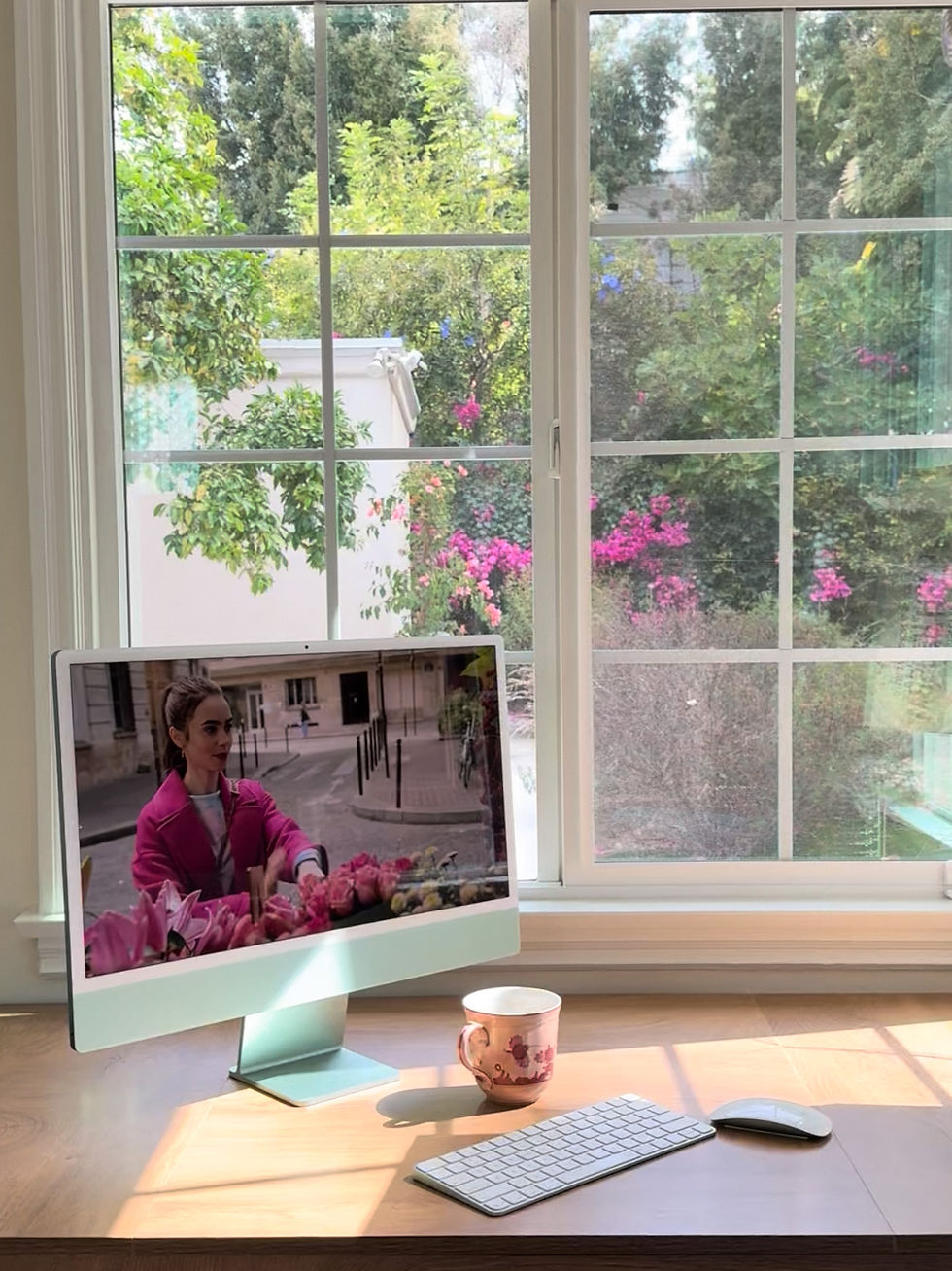 Sunlight across a wood desk with a pink floral teacup and a mint iMac playing Emily in Paris by a garden window