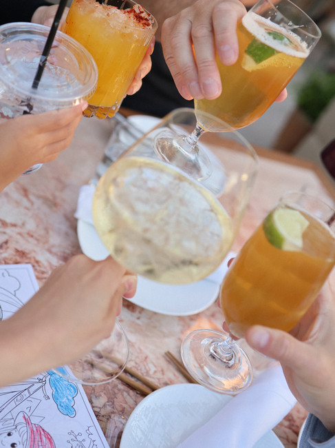 Four hands clinking colorful cocktails together over a marble table in a birthday toast