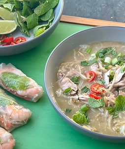 A bowl of pho, summer rolls and a platter of pho toppings