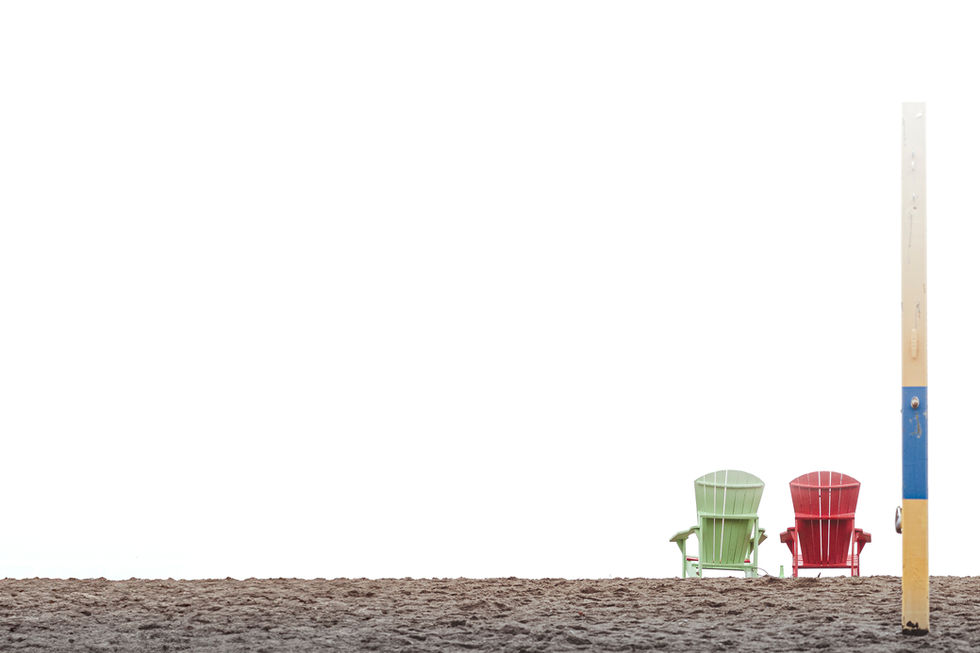 Two Muskoka chairs (one green, one red), rest on a calm sandy beach, with a blue and yellow shower stand in the foreground. 