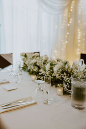 Wedding reception table setting with white flowers, glasses, and silverware ready.