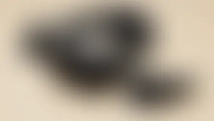 The Steam Frame VR headset in black, shown with its two matching controllers on a light beige surface. The headset has a soft fabric interior and an adjustable strap.