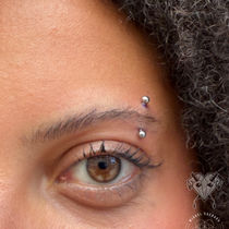 Close-up of a brown eye with a silver curved barbell in titanium eyebrow piercing placed along the outer brow line.