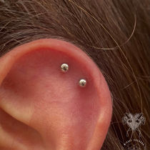 Close-up of a double helix piercing with two silver studs aligned on the upper outer ear cartilage.