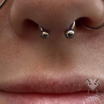 Close-up of a septum piercing with a titanium circular barbell centered beneath the nose.