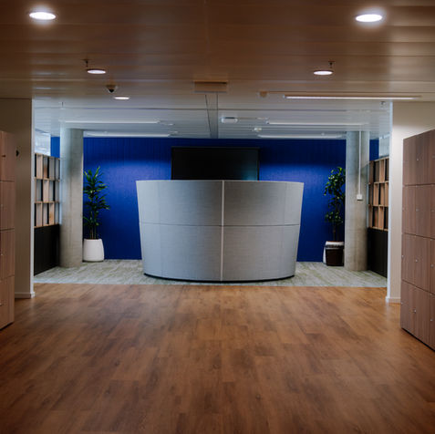 Hall d’accueil du projet SITA avec comptoir central, habillage bois et mur d’accent bleu.