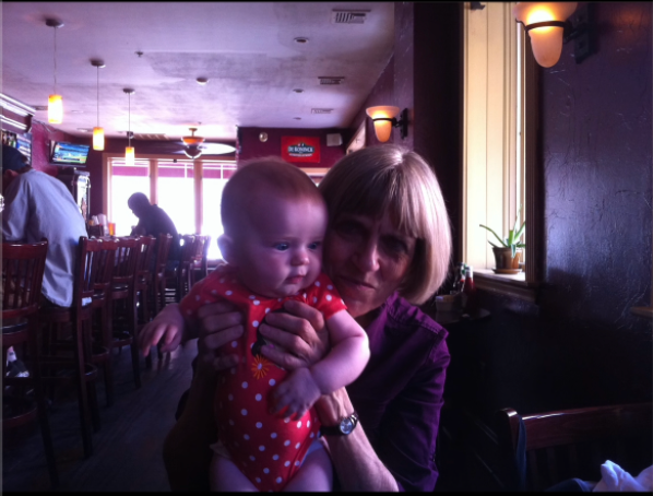 a polaroid of a grandmother holding a neborn in her hands in a booth at a diner
