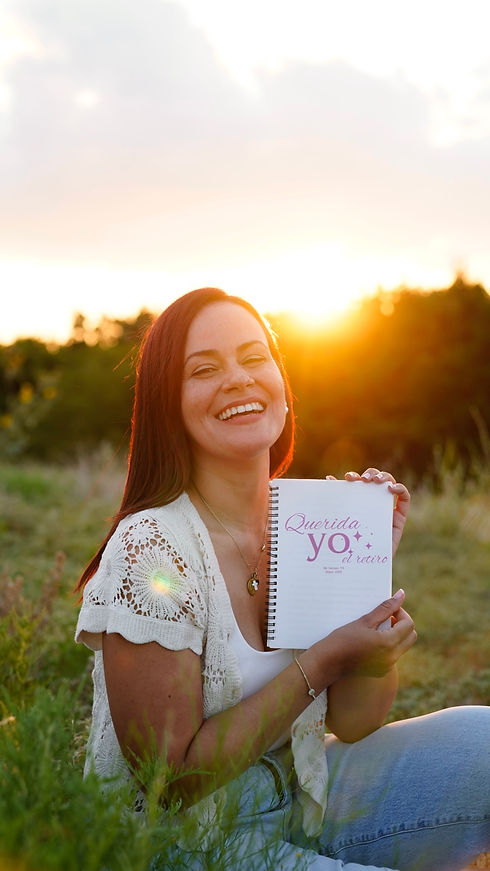 Mariam Reyes sonriendo al atardecer mientras sostiene su libreta “Querida Yo”, reflejando su enfoque amoroso y transformador en el acompañamiento emocional.