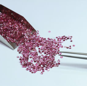 Loose pink gemstones spilling from tweezers onto a white background.