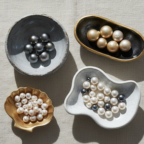 Black, gold, cream, and white pearls sorted by color in small ceramic dishes on linen