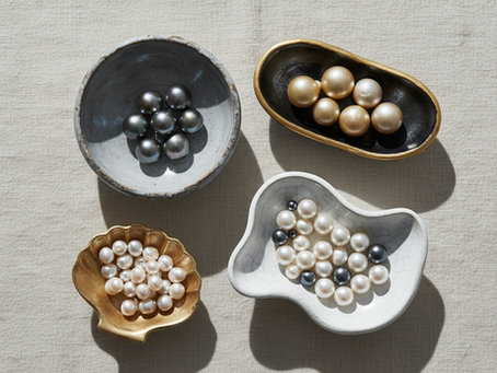 Black, gold, cream, and white pearls sorted by color in small ceramic dishes on linen