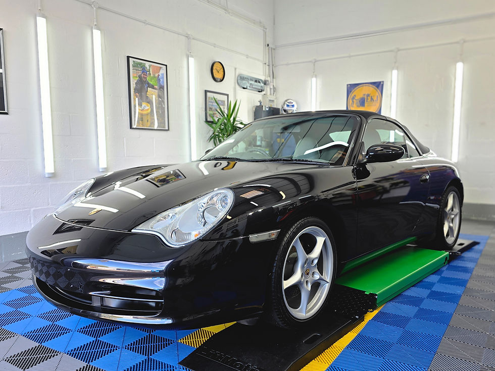 Black Porsche convertible on a green lift in a bright white showroom with blue floor tiles.