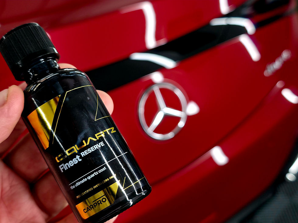 Hand holding a C.Quartz Finest Reserve bottle in front of a glossy red Mercedes badge and hood reflection.
