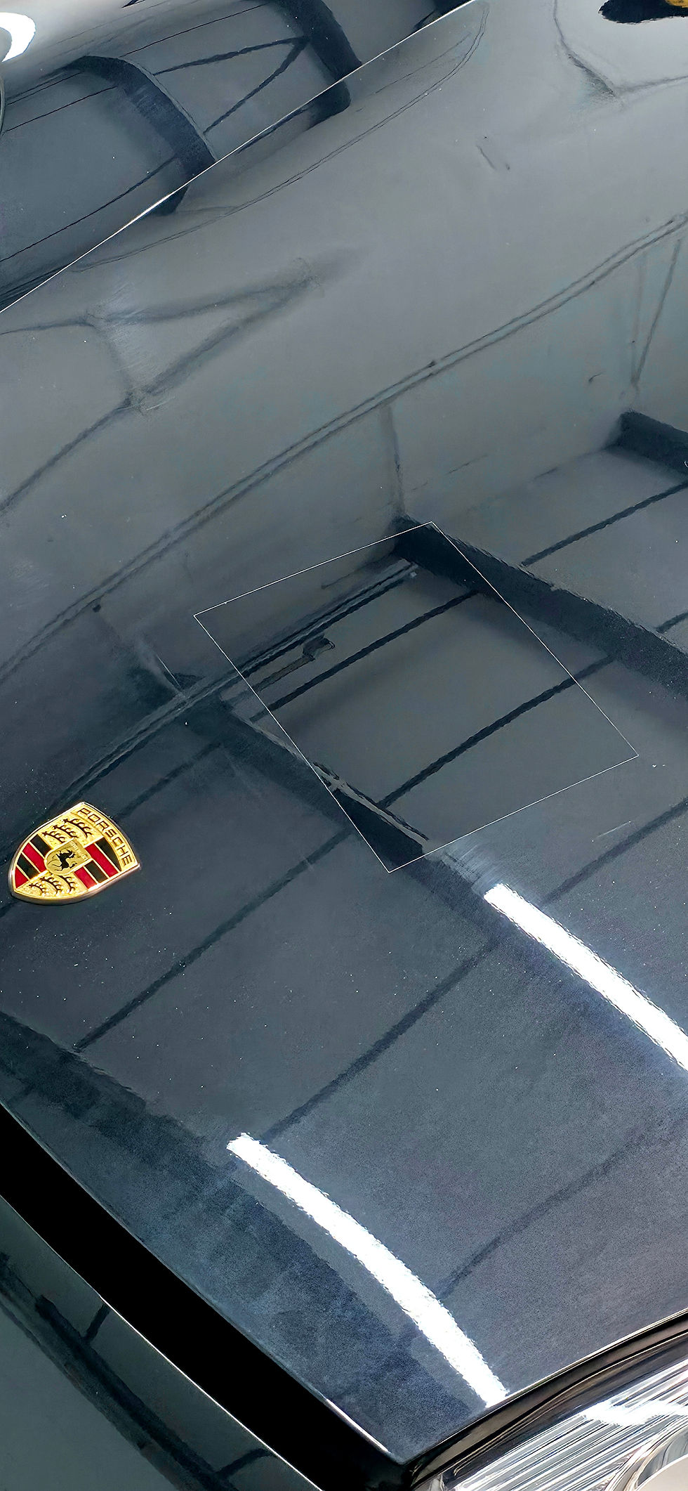 Glossy black Porsche hood with gold crest, reflecting overhead lights in a showroom or garage.