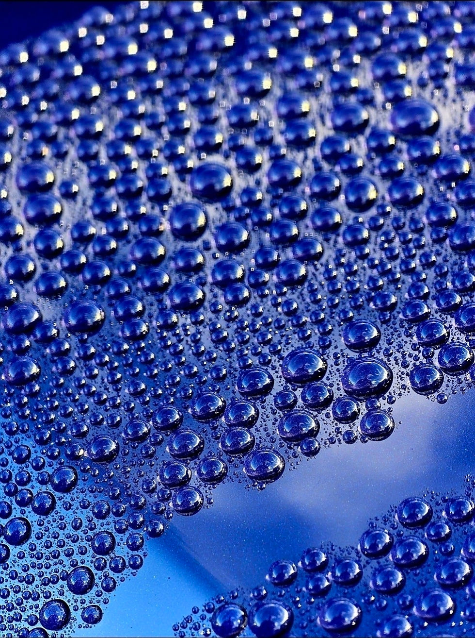 Macro of blue water droplets beading on a glass surface, sparkling against a cool blue background with no text.