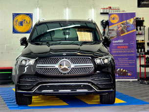 Black Mercedes SUV in a bright car detailing shop, with E.K.J. and CARPRO/RUPES banners and polished glossy reflections.