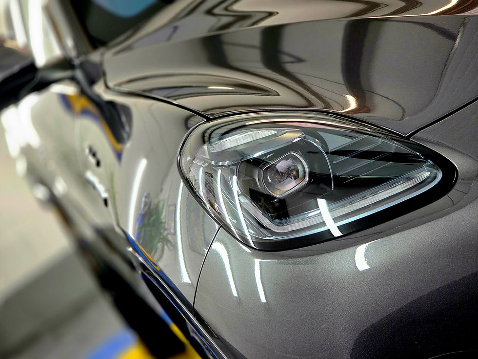 Close-up of a sleek gray car's headlight in a well-lit garage, with reflections on the polished surface and a modern design focus.
