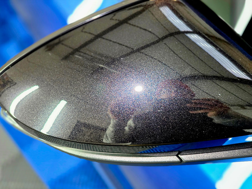 Close-up of a shiny car side mirror reflecting a person and ceiling lights. The setting is a garage with blue and gray tones.