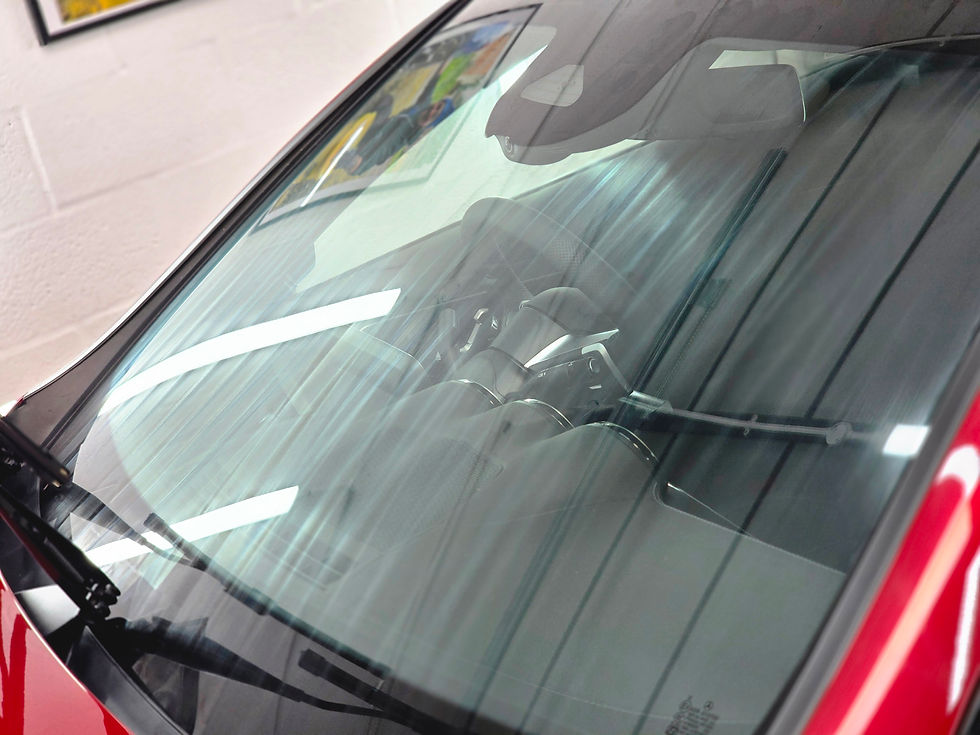 Close-up of a red car’s rear window and interior seats, with bright light reflections in a garage-like setting.