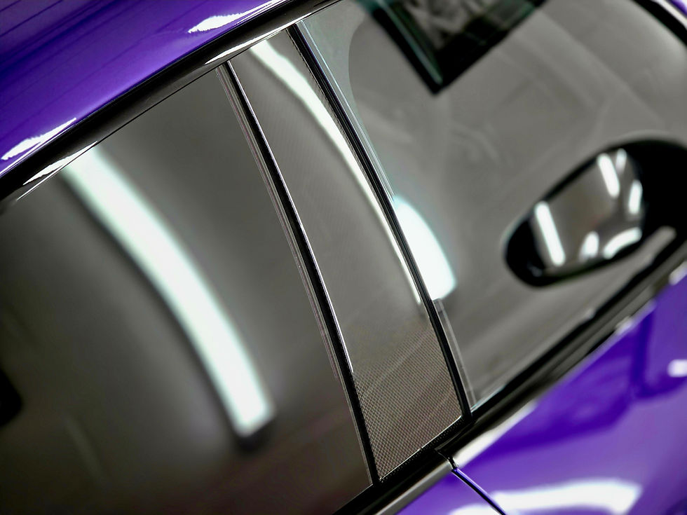 Close-up of a purple car’s glossy window pillar and chrome trim reflecting bright lights in a sleek showroom.