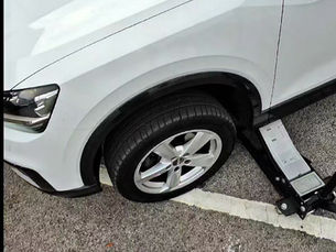 A alloy wheel being take off a white car with a car jack.