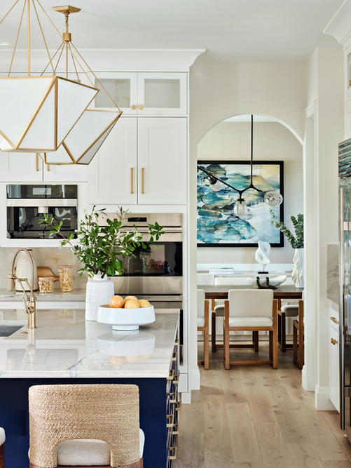 Kitchen with large island, white cabinetry, brass lighting, and view through arched opening into dining room.
