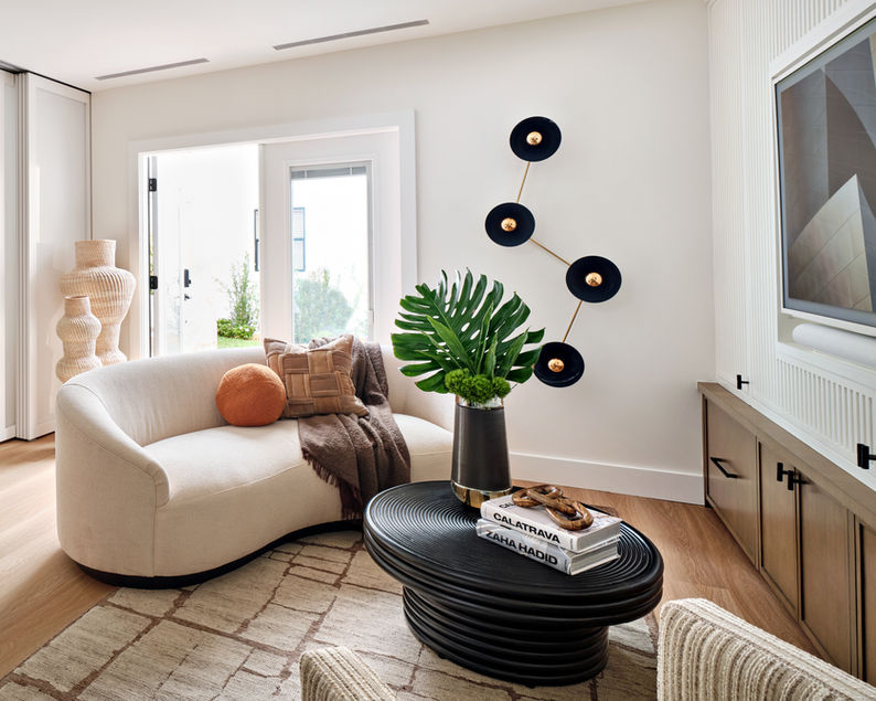 Guest house seating area with curved sofa, round coffee table, sculptural wall accents, and natural light.