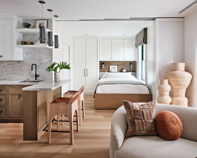 Open-concept guest suite with built-in bed, light wood flooring, compact kitchen, and sculptural decor.