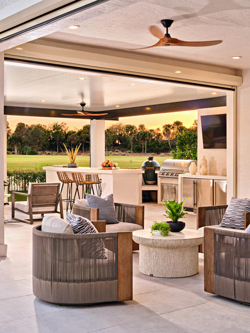 Covered outdoor living area with lounge seating, dining table, outdoor kitchen, ceiling fans, and open views to landscaped grounds.
