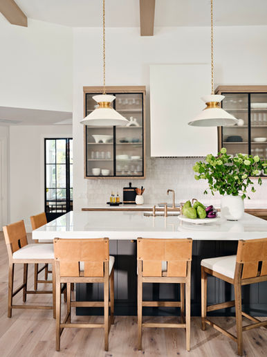 Kitchen island with wood bar stools, glass-front cabinets, pendant lighting, and open shelving in a bright, modern space.