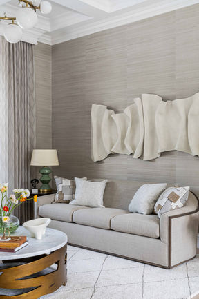 Living room with neutral sofa, sculptural wall art, textured wallcovering, and layered accessories.