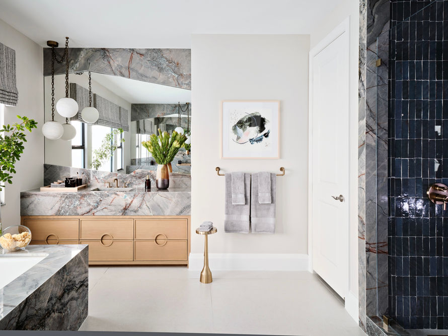 Primary bathroom with marble vanity, wood cabinetry, sculptural pendant lighting, and glass-enclosed dark tile shower.