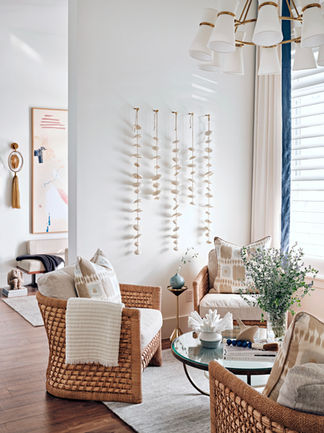 Sitting area with woven lounge chairs, sculptural wall art, glass tables, greenery, and natural light.